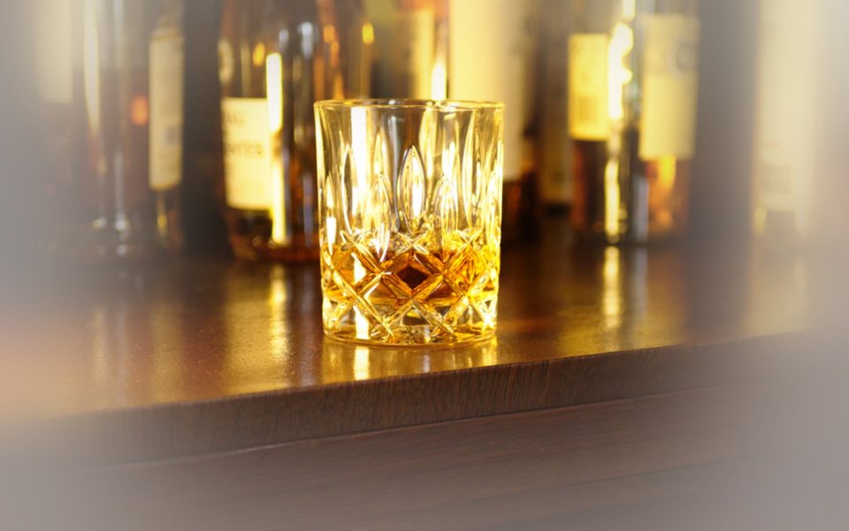 Zwei geschliffene Whiskygläser mit goldenem Destillat auf dunklem Grund